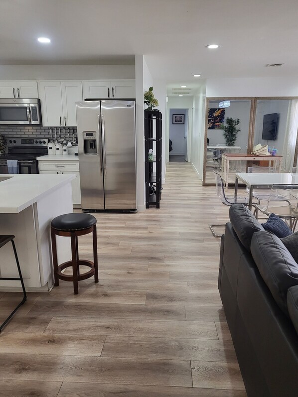 Una cocina moderna con electrodomésticos de acero inoxidable, piso de madera y un comedor con sofá y sillas.