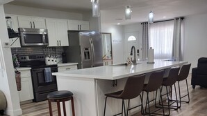Una cocina moderna con una isla central, electrodomésticos de acero inoxidable y un comedor con taburetes de bar.
