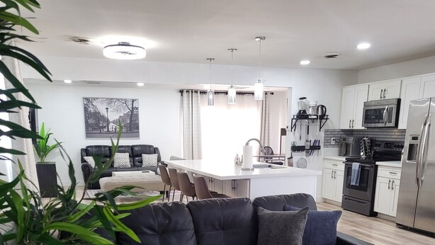 Una sala moderna con un sofá seccional negro, una mesa de centro de vidrio y un comedor con una mesa y sillas blancas.