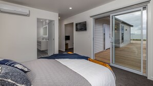 A bedroom with a bed, a bathroom, a TV, and a sliding glass door to an outdoor deck.