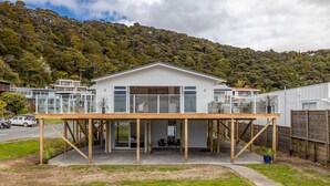 A modern house with a large deck, a covered patio, and a view of a lush green hill.