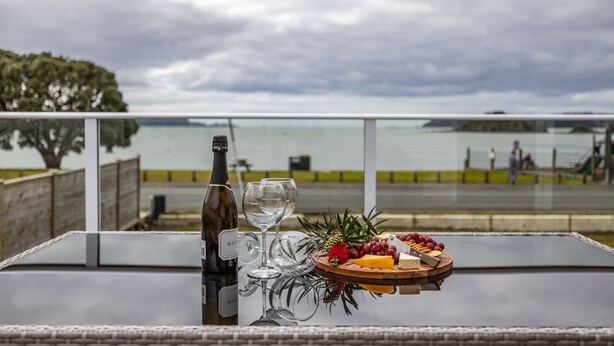 A table with a bottle of wine, a glass, and a wooden board with cheese and grapes.