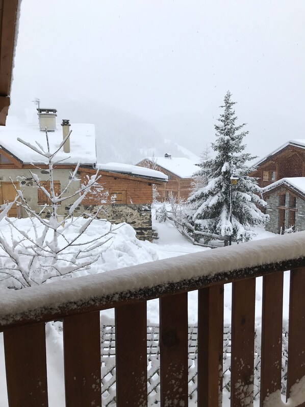 Une scène hivernale enneigée avec une balustrade en bois, un arbre recouvert de neige et des maisons en arrière-plan.