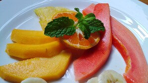 Ein weißer Teller mit geschnittenen Früchten, darunter Wassermelone, Orange, Mango und Banane.
