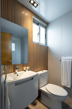 A modern bathroom with a wooden panel wall, a large mirror, a white sink, a toilet, and a towel hanging on the wall.
