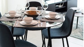 Un comedor moderno con una mesa redonda para cuatro comensales, sillas negras y una lámpara colgante original con bombillas expuestas.