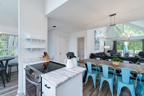A modern kitchen with a built-in stove, a marble countertop, and a dining area with blue chairs and a wooden table.