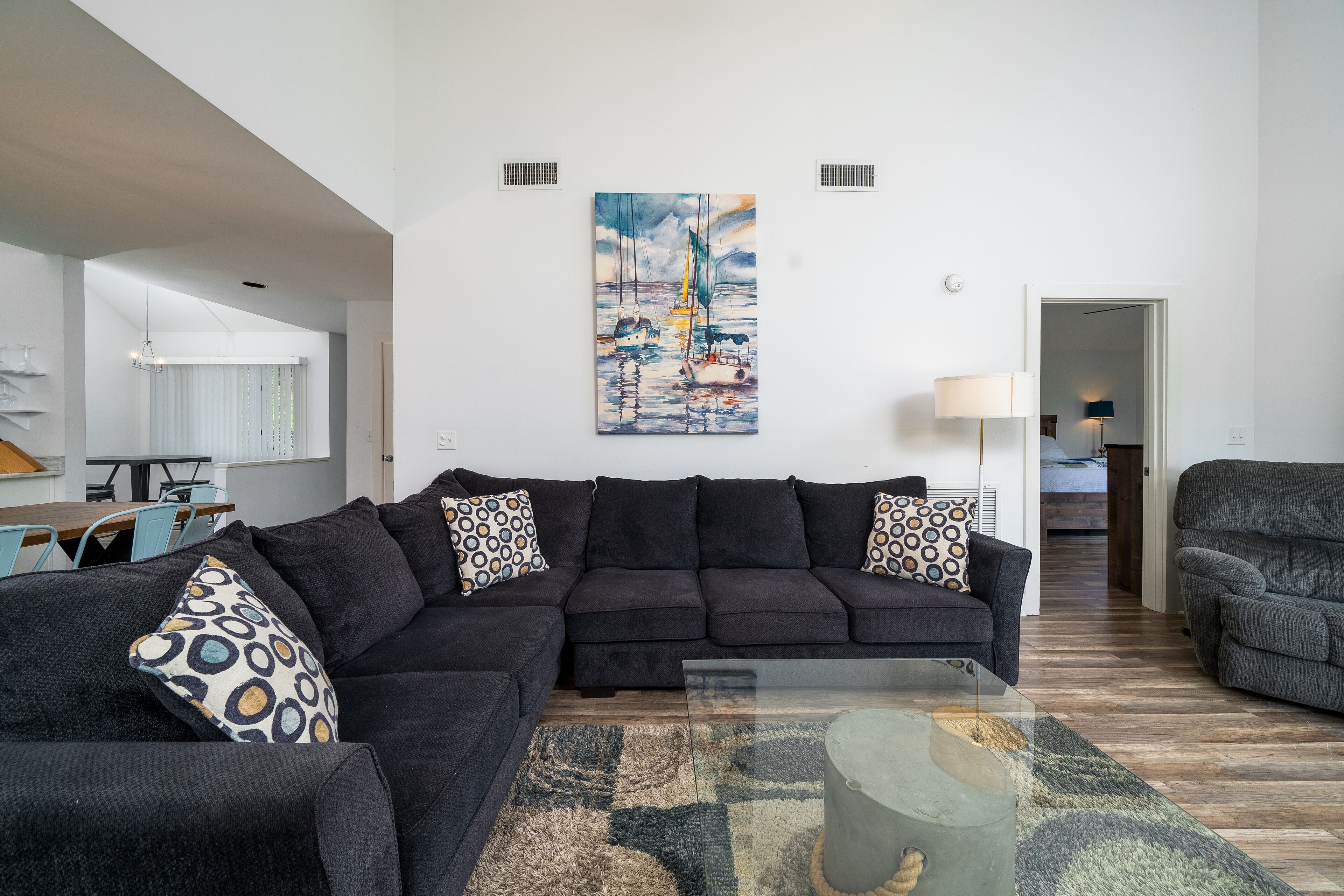 A modern living room with a sectional sofa, a glass coffee table, and a painting of sailboats on the wall.