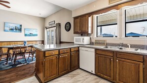 A kitchen with wooden cabinets, a microwave, a dishwasher, and a dining area with chairs and a table. - High Tide - A Fisherman's Delight:  4 BR Channel Home w/ Boat Ramp in Cherry Grove (North Myrtle Beach)