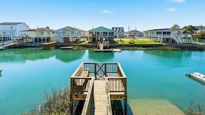 A waterfront property with a dock, multiple houses, and a grassy area. - High Tide - A Fisherman's Delight:  4 BR Channel Home w/ Boat Ramp in Cherry Grove (North Myrtle Beach)