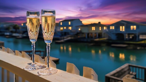 Two glasses of champagne on a wooden deck with a marina and houses in the background. - High Tide - A Fisherman's Delight:  4 BR Channel Home w/ Boat Ramp in Cherry Grove (North Myrtle Beach)