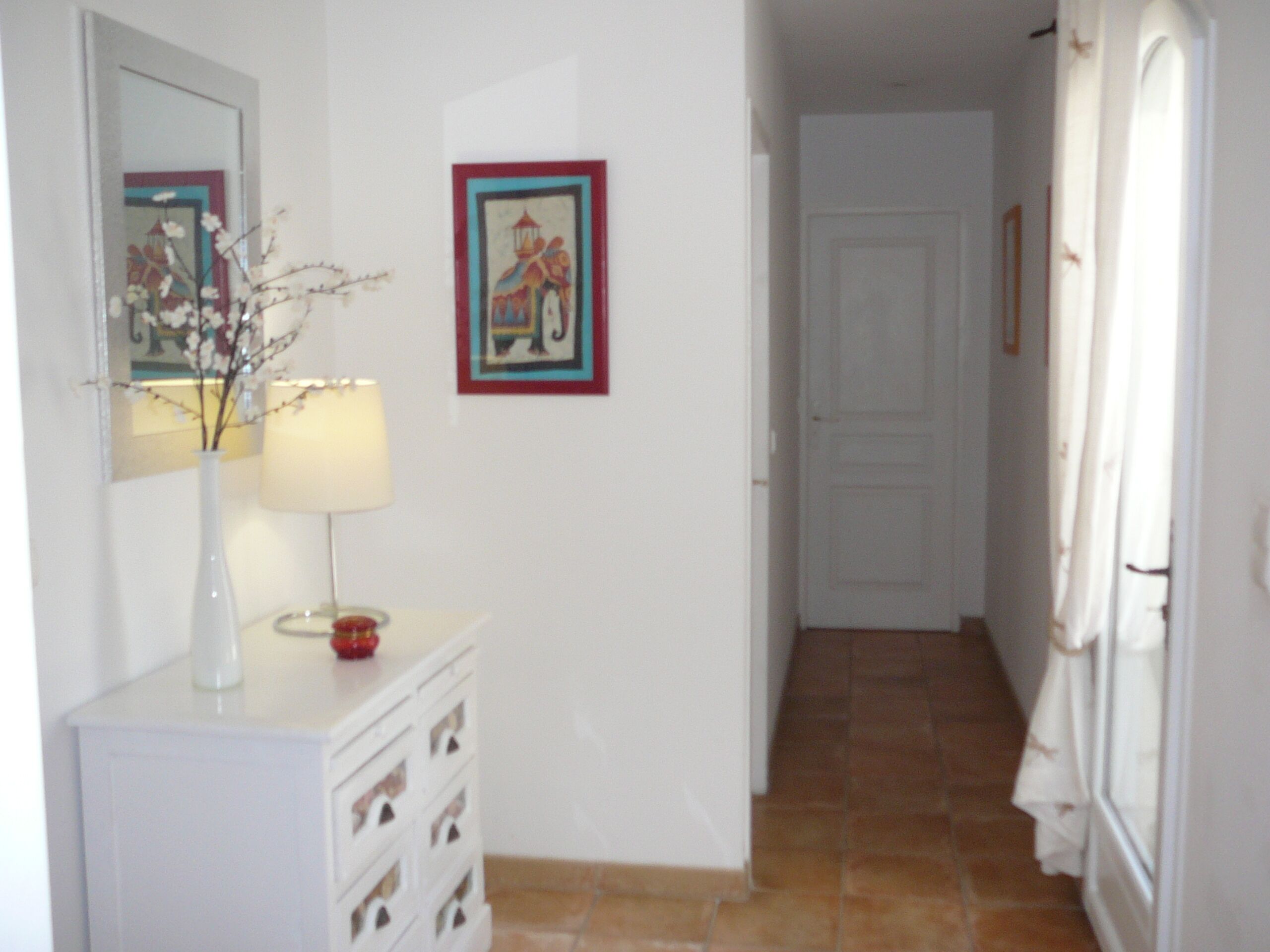 A hallway with a white dresser, a mirror, a vase with flowers, and a framed picture on the wall.