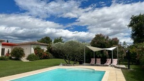Una piscina con agua cristalina azul, rodeada por un césped cuidado y una zona de patio con mobiliario exterior.
