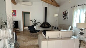 Una sala de estar con sofá, sillón, una mesa de vidrio con objetos decorativos, chimenea y televisor.