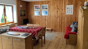 A cozy room with wooden walls, a dining table with a red tablecloth, a red sofa, and a small wooden cabinet.