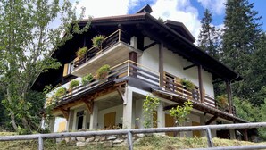 A traditional chalet with multiple balconies, stone walls, and a wooden railing in front.