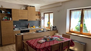 A compact kitchen with wooden cabinets, a dining table with a red tablecloth, and a window with curtains.