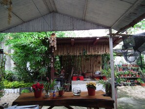 Un espacio al aire libre techado con una mesa de madera, varias plantas en macetas y un adorno colgante.