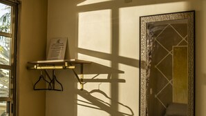 A room with a wooden bench, an air conditioning unit, a wall-mounted mirror, and a window casting shadows.