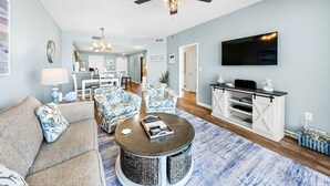 Ein Wohnzimmer mit Deckenventilator, Fernseher, Couchtisch und Möbeln mit Muster.