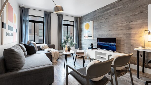 Ein modernes Wohnzimmer mit grauem Sofa, einem Couchtisch und einem Fernseher an einer Holzwand.