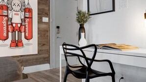 Een moderne kamer met een wit bureau, een zwarte stoel, een vaas met planten en een kunstwerk in een lijst aan de muur.