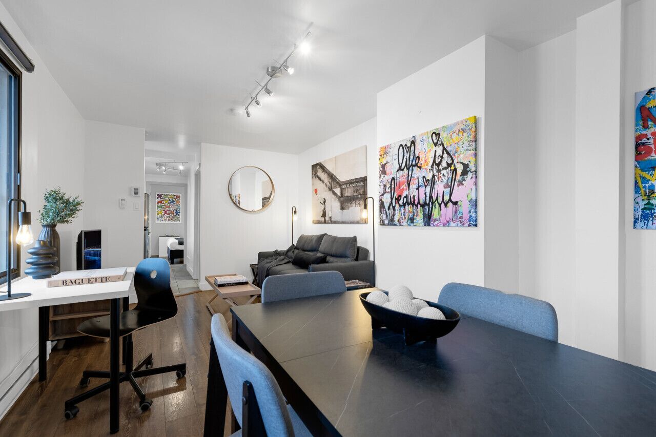 A modern living room with a dark dining table, blue chairs, a sofa, and a large abstract painting.