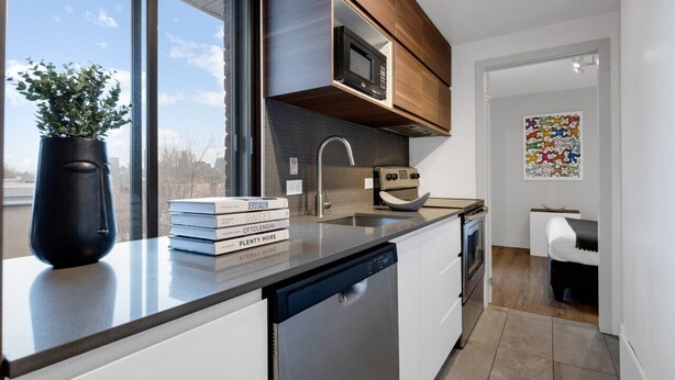 Eine moderne Küche mit eingebautem Geschirrspüler, Mikrowelle und Spüle. Ein Fenster bietet Blick auf die Stadt, und es gibt eine kleine Essecke mit Tisch und Stühlen.