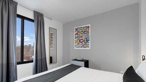 Ein modernes Hotelzimmer mit einem großen Bett, einem Nachttisch, einem Spiegel und zwei abstrakten Bildern an der Wand.