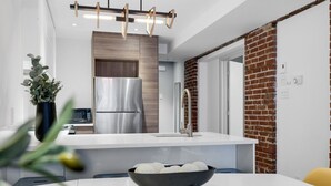 Eine moderne Küche mit weißer Arbeitsplatte, Edelstahlgeräten und einer Wand in Backsteinoptik.