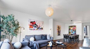 A modern living room with a grey sofa, a dining table with chairs, and a large plant. - LiV MTL Soho Spacious Rooftop Suites for Groups Near Downtown Montreal (Montréal)