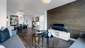 Een moderne woonkamer met een flatscreen televisie, een eethoek en een keuken op de achtergrond.
