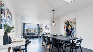 Een moderne eetruimte met een lange tafel, zwarte stoelen en een witte tafelvoet. Achtergrond is een groot raam en de kamer heeft een minimalistisch design met witte muren en een houten vloer.