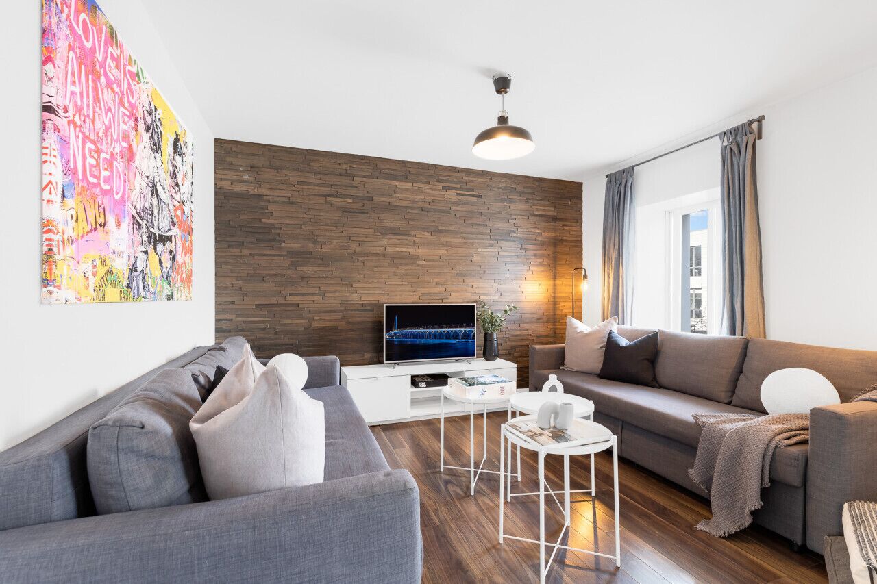A modern living room with a wooden accent wall, a flat-screen TV, and a large abstract painting.