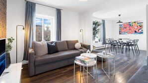 Uma sala de estar moderna com um sofá cinzento, uma mesa de centro e um espaço de jantar com mesa e cadeiras.