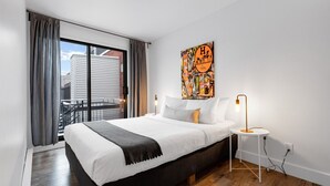 Ein Schlafzimmer mit einem Bett, einem Nachttisch, einer Lampe und Blick auf Gebäude.