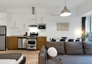 A modern kitchen with white cabinets, stainless steel appliances, and a dining area with a gray sofa and table.