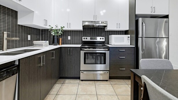 A modern kitchen with stainless steel appliances, dark wood cabinets, and a tiled backsplash. - Spacious 4BR rooftop near Downtown (Montréal)