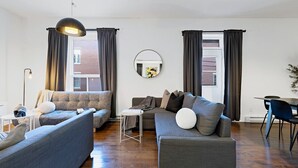 A modern living room with a sofa set, a dining table, and a round mirror on the wall. - Spacious 4BR rooftop near Downtown (Montréal)