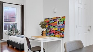 A bedroom with a bed, a desk, a chair, a window with curtains, a door, and a wall with a colorful artwork. - Spacious 4BR rooftop near Downtown (Montréal)