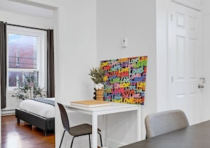 A bedroom with a bed, a desk, a chair, a window with curtains, a door, and a wall with a colorful artwork. - Spacious 4BR rooftop near Downtown (Montréal)