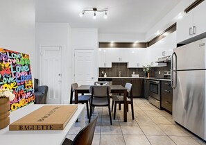 Una cocina moderna con armarios blancos, electrodomésticos de acero inoxidable y una zona de comedor con mesa y sillas.