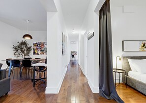 Un interior moderno con comedor, un pasillo que lleva a un dormitorio y un ventanal con cortinas.
