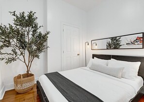 A bedroom with a bed, a potted plant, a door, and a framed picture on the wall.