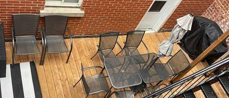 Um terraço no telhado com mesa e cadeiras, piso de madeira e parede de tijolos.