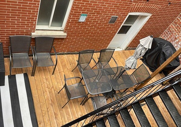 Una terraza en la azotea con una mesa y sillas, piso de madera y pared de ladrillo.