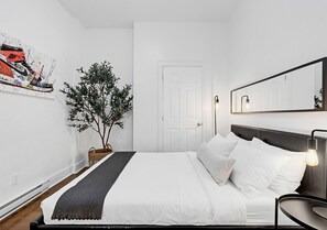 Ein ordentlich eingerichtetes Schlafzimmer mit Bett, Nachttisch und einem wandmontierten Spiegel.