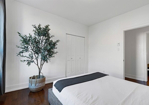 Un dormitorio con cama, una planta en maceta y un armario blanco.