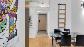 Un espace repas moderne avec une table en verre, des chaises noires et une échelle en bois adossée au mur.