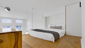 A modern bedroom with a wooden floor, a white bed with gray pillows, a wooden desk, and a grid-patterned wall. - LiV MTL Main Plateau Urban Suites Near Downtown Montreal (Montréal)